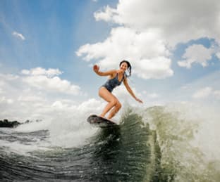 woman surfing on a wake board behind a wake boat